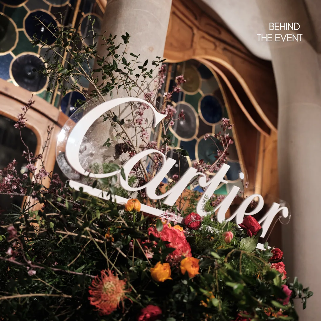 Rótulo de Cartier en letras de luz entre una instalación floral, con vidrieras modernistas al fondo.